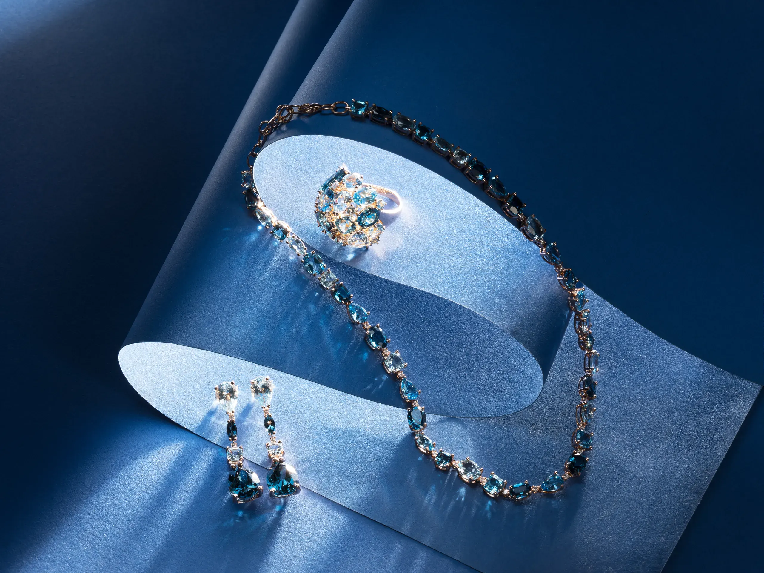 Iris necklace, ring and earrings with London Blue and Sky Blue topaz on blue paper – Ponte Vecchio Gioielli
